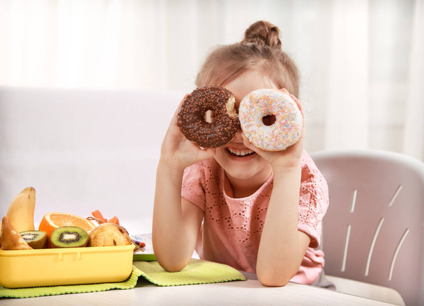 Pequeña hermosa chica alegre comiendo un donut
 - Foto, Imagen