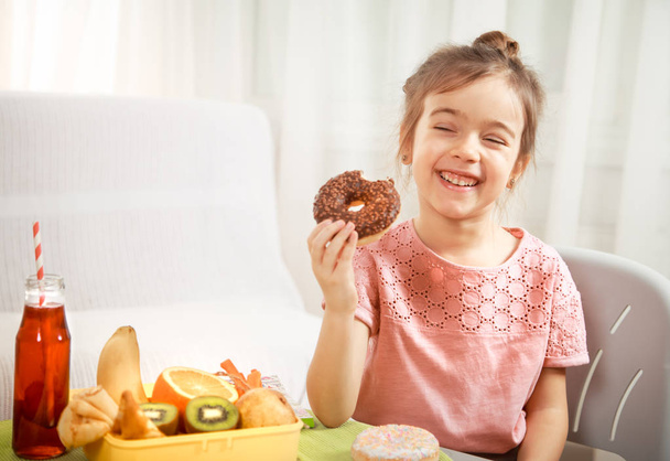 Pieni kaunis iloinen tyttö syö donitsin
 - Valokuva, kuva