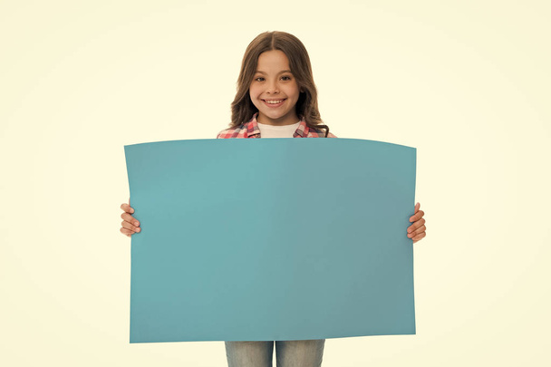 Children market advertisement. Girl kid holds blue blank surface copy space. Advertisement concept. Child cute girl looking happy while carries blue paper. Kid cheerful face sincere recommendation - Фото, зображення