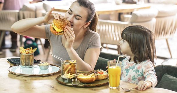 Mom with a cute daughter eating fast food in a cafe - Fotografie, Obrázek