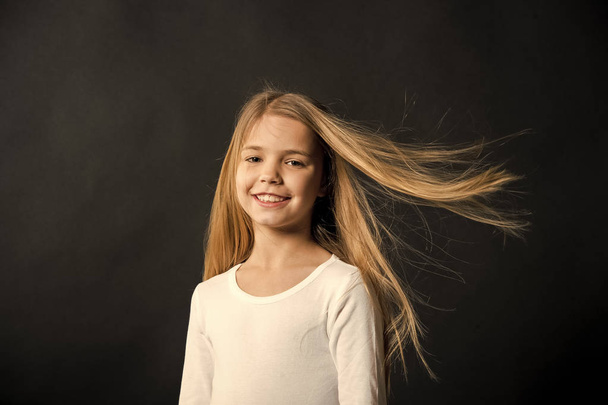 Little girl smile with long blond hair on black background. Happy child with fashion hairstyle. Beauty kid smiling with adorable look. Beauty salon. In this salon we love hair - 写真・画像