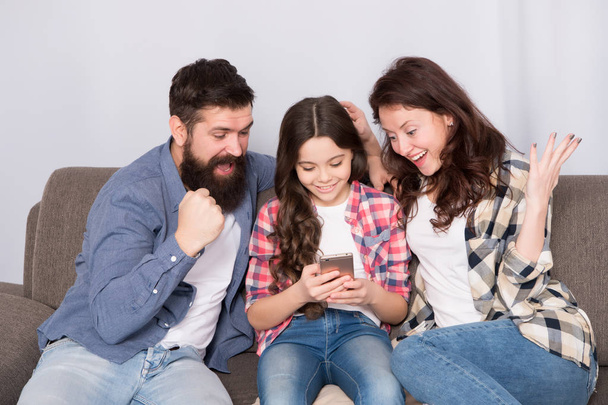 Child share news with mother and father. Little girl child use mobile phone with parents. Happy family at home. Child with childhood happiness. bearded man and woman with child. So much fun - 写真・画像