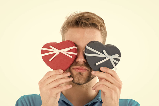 Guess which one. Man holds two heart shaped gift boxes in front of eyes, white background. Macho prepared romantic surprise for valentines day. Valentines day gift. Romantic surprise for her - Foto, imagen