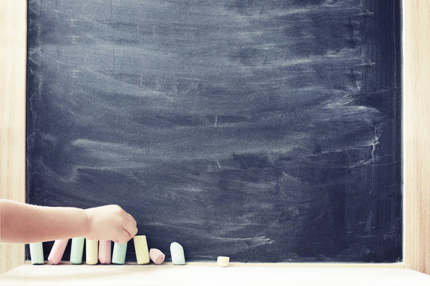 Χέρι του παιδιού λαμβάνοντας παστέλ χρωματιστά κομμάτια κιμωλία σε μαυροπίνακα σχολείο έννοια - Φωτογραφία, εικόνα
