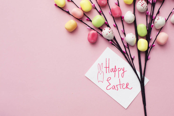 Handmade willow twigs with colorful Easter eggs decoration with greeting card on beige background - Fotó, kép