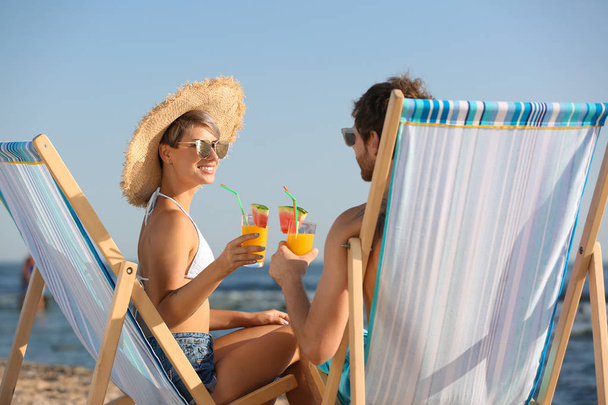 Young couple with cocktails in beach chairs at seacoast - Photo, image