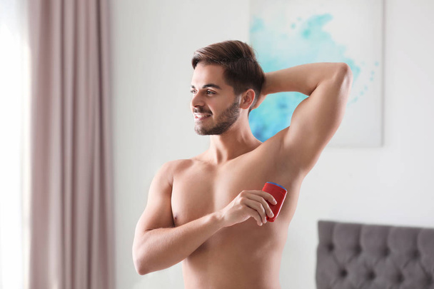 Handsome young man applying deodorant in room - Foto, Imagem