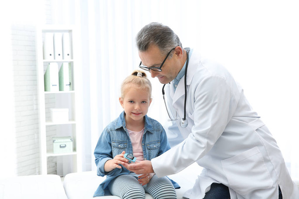 Arzt überprüft Puls des kleinen Mädchens mit medizinischem Gerät im Krankenhaus - Foto, Bild