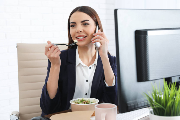 Office employee having salad for lunch while talking on phone at workplace. Food delivery - Фото, зображення