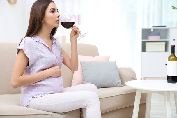 Future mother drinking wine from glass at home. Alcohol abuse during pregnancy - Foto, imagen