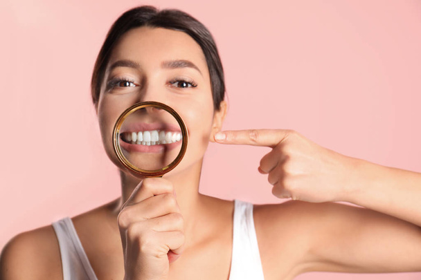 Young woman with healthy teeth and magnifier on color background - Photo, Image