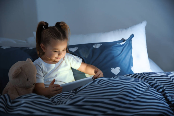 Beautiful little girl with gadget and toy in bed at night. Bedtime schedule - Фото, зображення