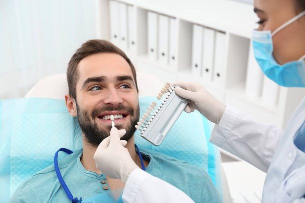Dentist matching young man's teeth color with palette in office - Foto, immagini