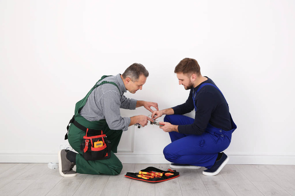 Senior electrician helping trainee stripping wire ends indoors - 写真・画像