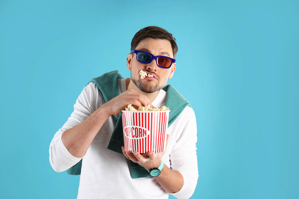 Man with 3D glasses eating tasty popcorn on color background - Foto, immagini