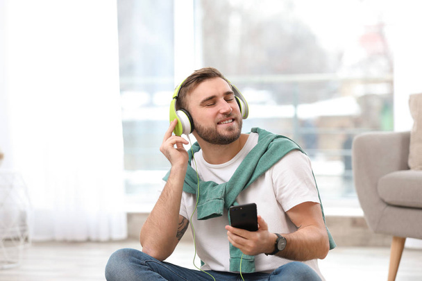 Young man with headphones and mobile device enjoying music in living room - Fotoğraf, Görsel