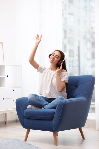 Mujer joven con auriculares descansando en sillón en casa
 - Foto, imagen
