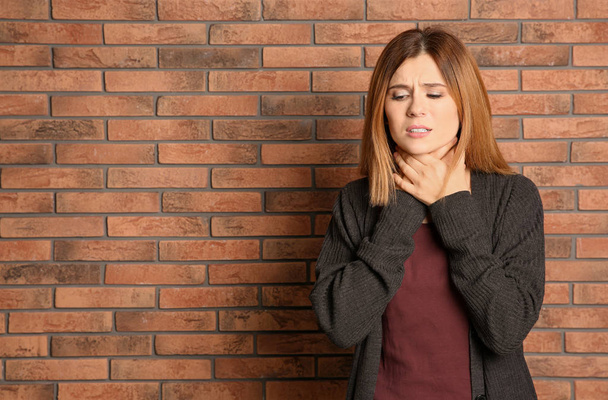 Woman suffering from cough near brick wall. Space for text - Photo, Image