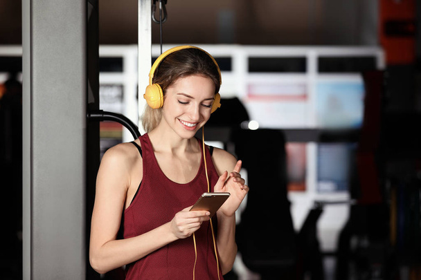 Young woman with headphones listening to music on mobile device at gym - Foto, afbeelding