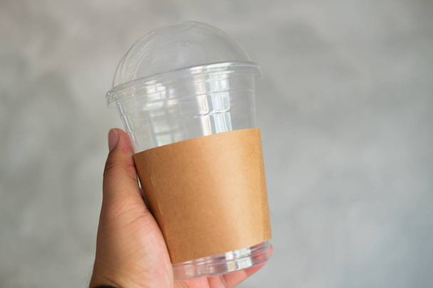 Άνθρωπος που κρατά πλαστικό ποτήρι μίας χρήσης ποτήρι με καφέ χαρτί μανίκι - Φωτογραφία, εικόνα