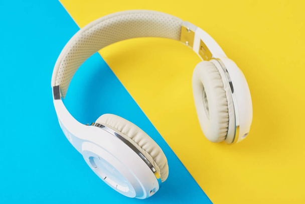 White wireless headphones on a blue and yellow background - Fotografie, Obrázek