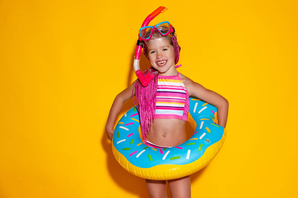 happy child girl in swimsuit with swimming ring donut on colored - Foto, Bild