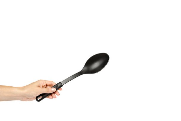 Hand met zwarte kunststof keuken lepel, keukengerei om te koken - Foto, afbeelding