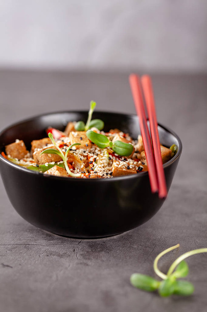 The concept of Japanese cuisine. Vegetarian noodles with tofu cheese and vegetables in a black ceramic plate. Red Chinese sticks. copy space - Fotografie, Obrázek