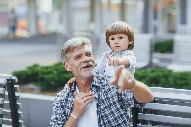 Grandfather showing something interesting to boy on bench near building - Photo, Image