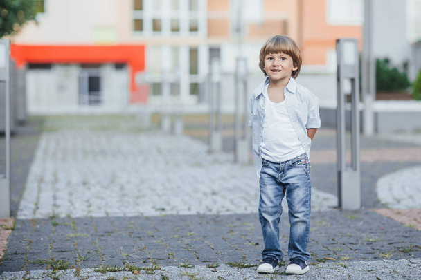 Happy laughing boy dressed at blue shirt and jeans walking down road and looking at camera - Foto, Bild
