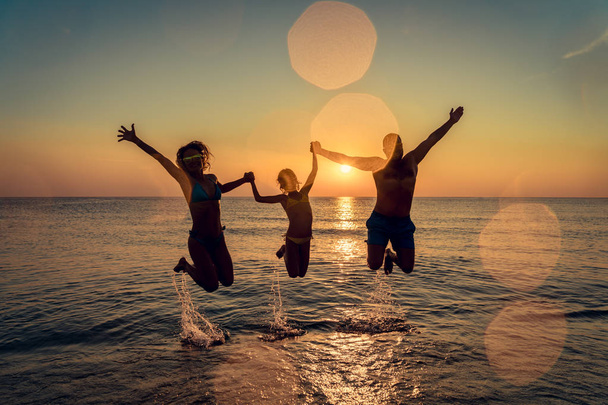 幸せな家族が海でジャンプします。人々 は屋外の楽しい時を過します。夏休みと健康的なライフ スタイルのコンセプト. - 写真・画像