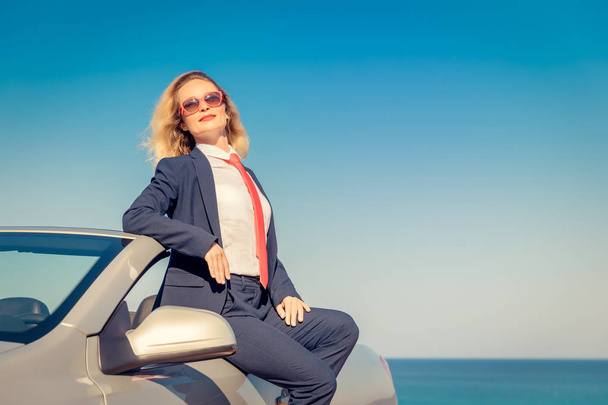 Successful young businesswoman on the beach. Woman sitting on the cabriolet classic car. Summer vacations and freedom travel concept - Zdjęcie, obraz
