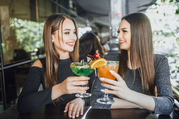 Young women sitting on summer terrace of modern cafe and drinking cocktails  - Фото, изображение