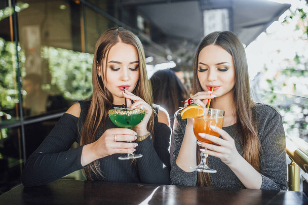 Young women sitting on summer terrace of modern cafe and drinking cocktails  - Photo, image