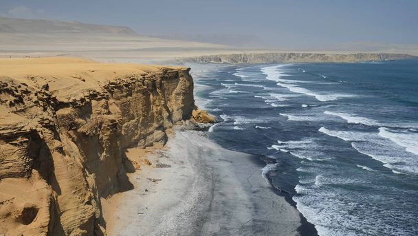 Scenic landscape - deep blue waters of Pacific Ocean with white waves and yellow clay high cliffs and rocky shore with desert in the background.Paracas National Park, Peru. - Photo, Image