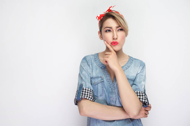 thoughtful beautiful young woman in casual blue denim shirt with makeup and red headband looking away and thinking isolated on white background. - Photo, image