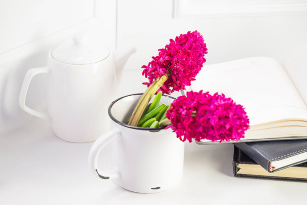 Servicio de té blanco sobre fondo blanco, junto a una taza grande de metal blanco con flores de jacinto rosa. En el fondo hay una pila de cuadernos. Concepto de buenos días y primavera
 - Foto, imagen