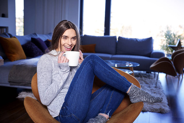 Ritratto di giovane donna felice che prende una tazza di tè mentre si rilassa sul divano di casa
.  - Foto, immagini