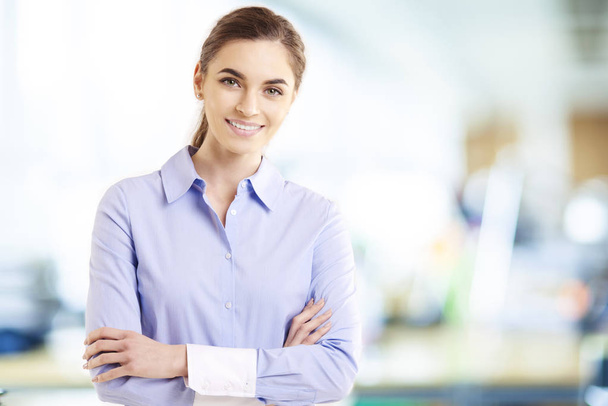 Portrait shot of beautiful businesswoman wearing shirt while standing with arms crossed in the office.  - Foto, Imagen