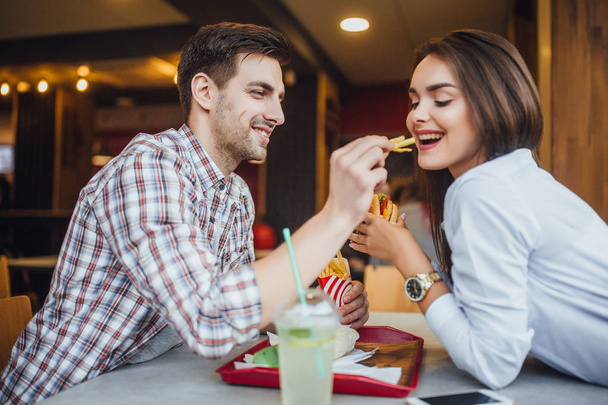 young couple having fun in fast food restaurant, man feeding woman fries - Photo, Image