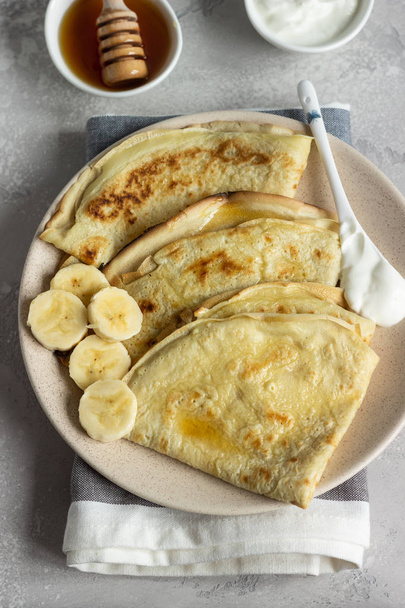 Thin pancakes or crepes with natural yogurt, honey and banana on a plate. Light concrete background. Copy space. - Φωτογραφία, εικόνα