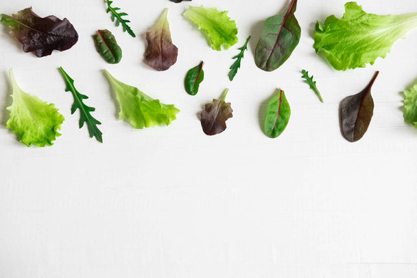 Green salad leaves on a white background. Pattern with lettuce leaves. Background design with leaves for salad. Pattern with lettuce leaves. Slimming, vegetarianism, organic food - 写真・画像