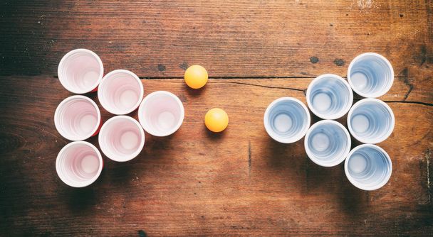 Beer pong. Kelímky plastové červené a modré barvy a ping pong míčky na dřevo, horní pohled - Fotografie, Obrázek