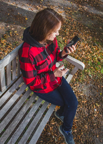 Jolie brune de 50 ans, assise sur un banc avec un mobi
 - Photo, image
