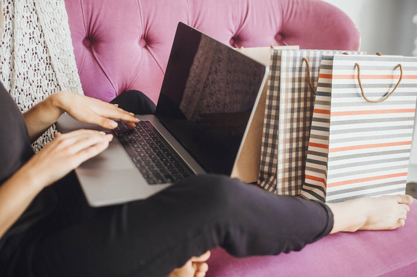 young beautiful woman online shopping for laptop on modern sofa with gift bags - Fotoğraf, Görsel