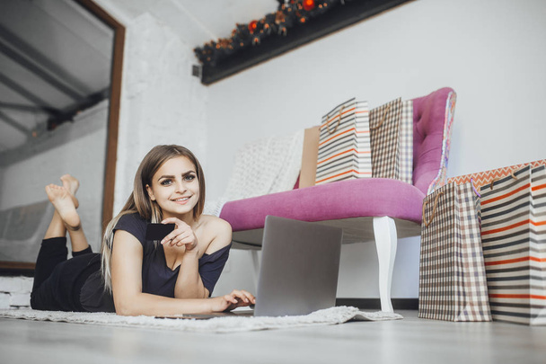 Young beautiful woman holding credit card and using laptop at home on floor - Photo, Image