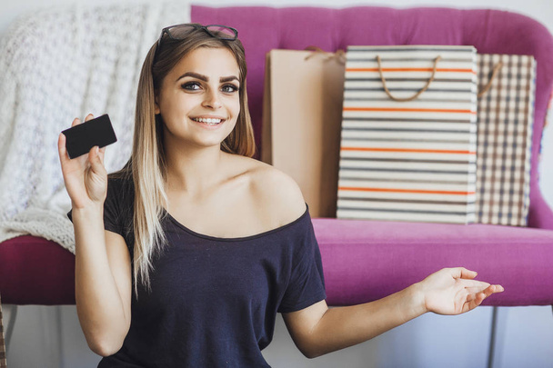 young beautiful woman holding credit card in hands and showing on gift bags after shopping  - Фото, зображення