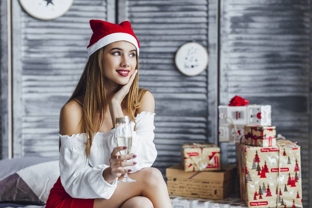 クリスマスの帽子をかぶった女性が寝室でシャンパンを飲み - 写真・画像