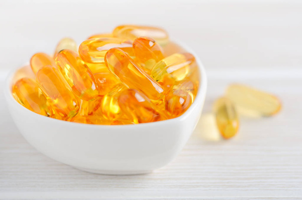Fish oil capsules on a white wooden background, vitamin D supplement, selective focus. - Photo, Image