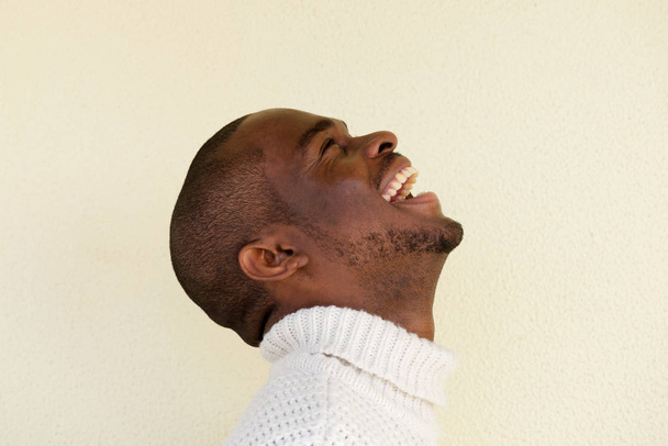 Close up side portrait of handsome african american man in sweater laughing and looking up - Photo, Image